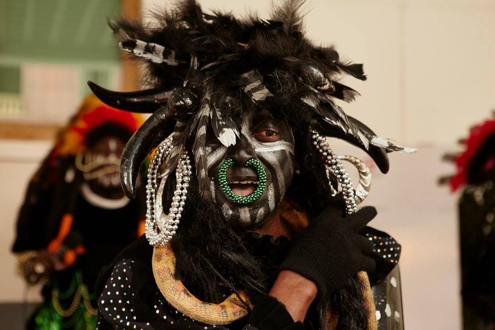 A person representing Black Indians wearing a feathered headdress, face paint, and a green nose ring.