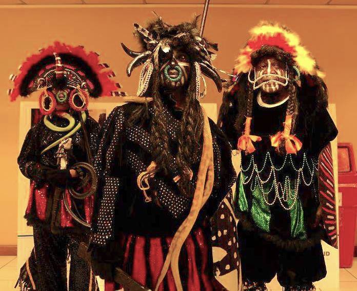 Three Black Indians in elaborate traditional ceremonial costumes, masks, and face paint perform war chants.