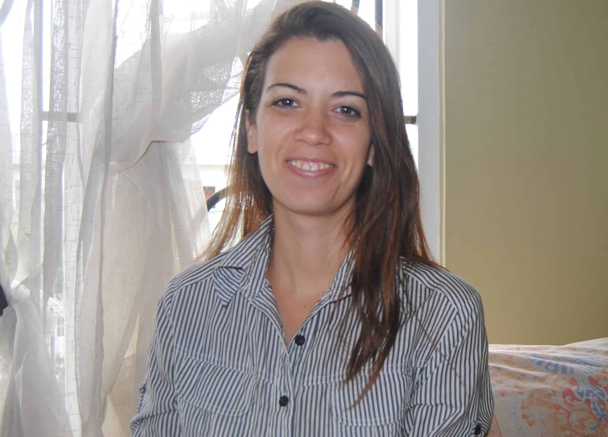 Carolina Arrieta Castillo smiles at the camera, wearing a blue and white striped button-down shirt with her long brown hair down.