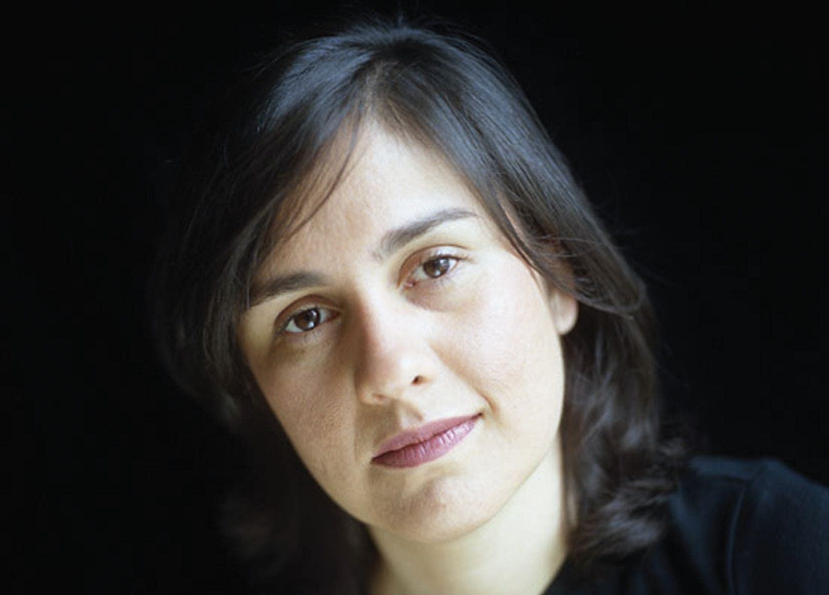 Headshot of author Kamila Shamsie looking towards the camera against a black background.