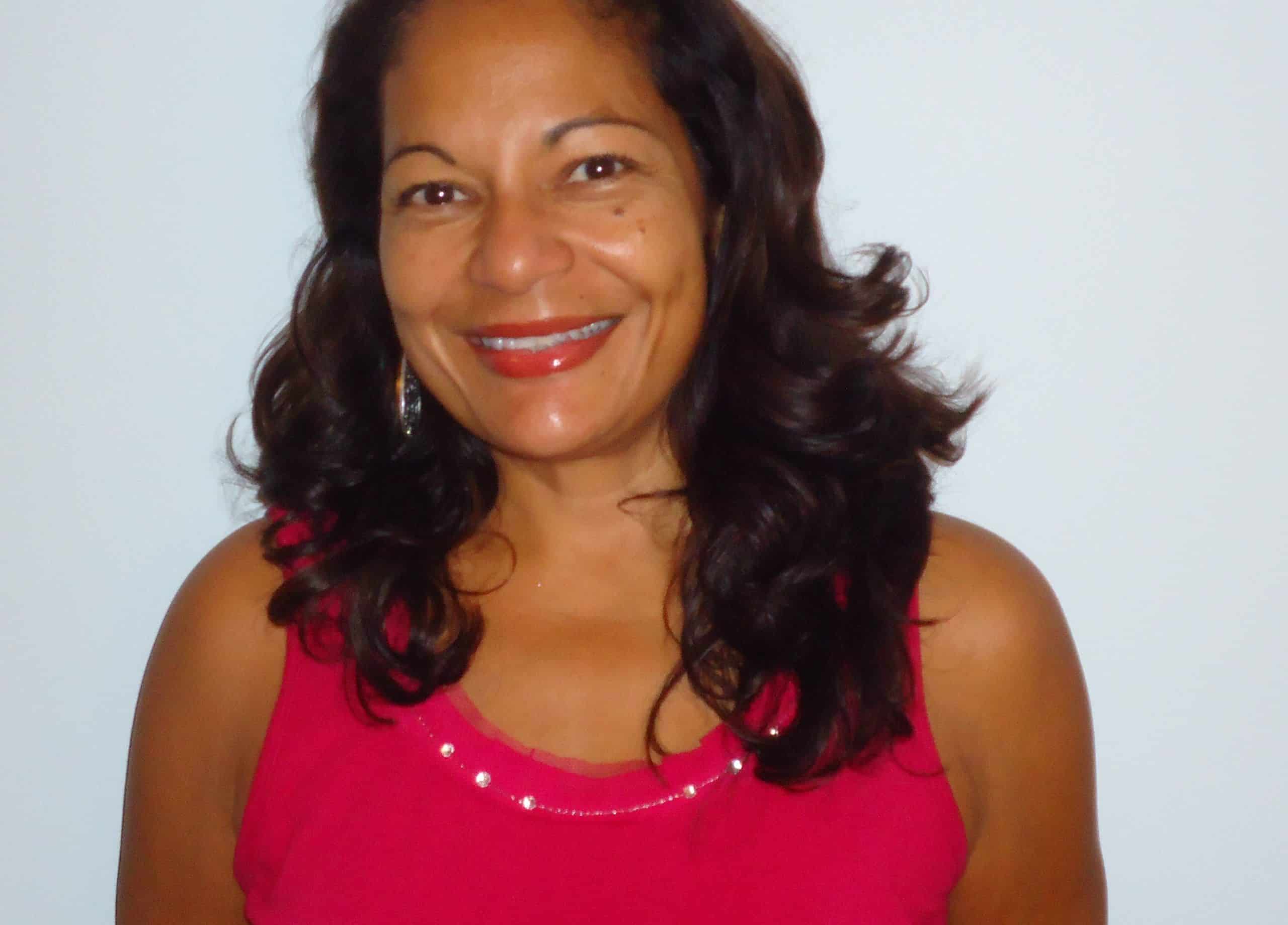 A smiling woman with dark wavy hair wearing a red sleeveless top.