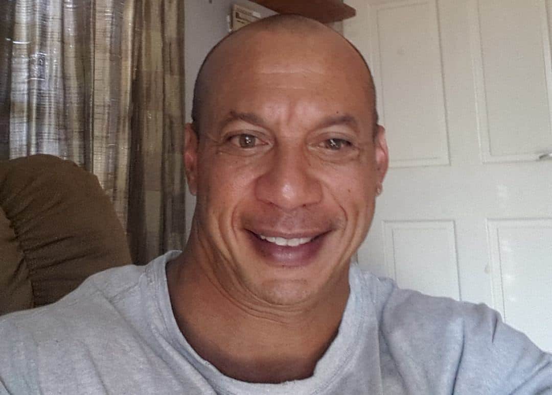 Ty N. Batson is a smiling man with a shaven head, wearing a grey t-shirt.