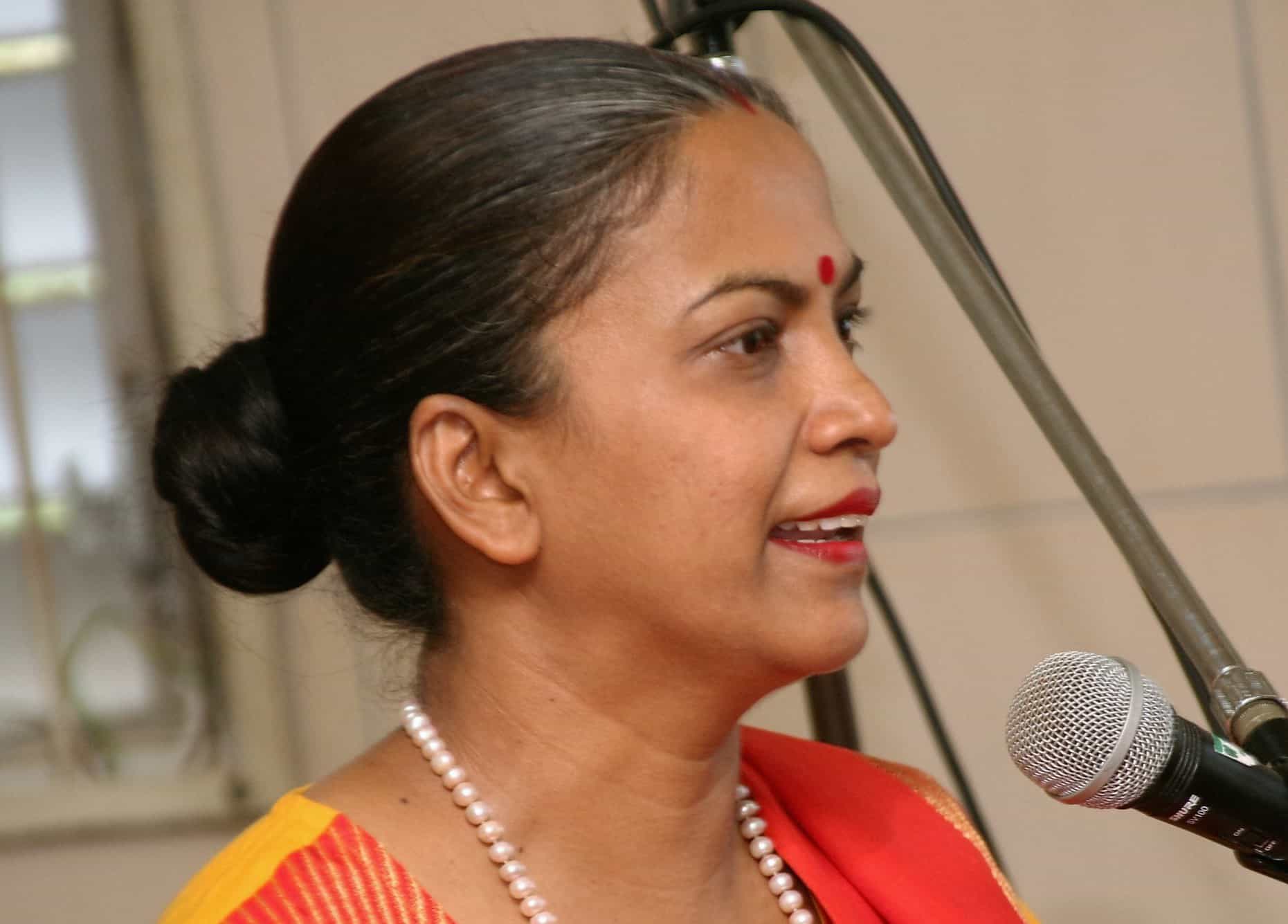 Geeta Ramsingh, wearing a bindi and a pearl necklace, speaks into a microphone.
