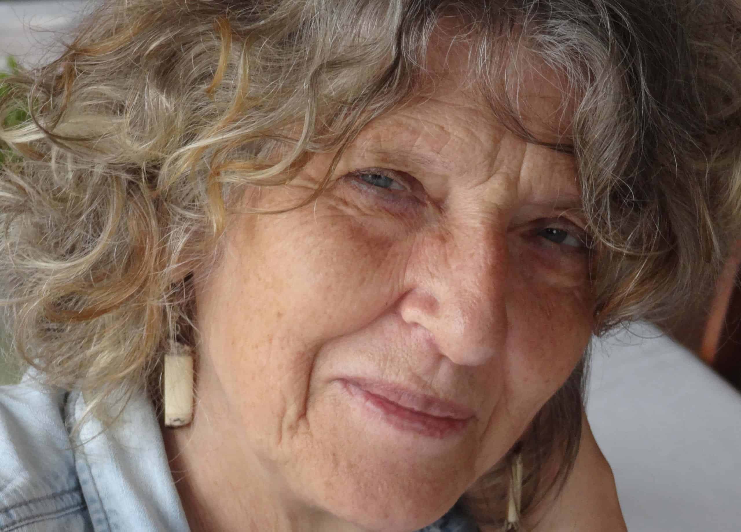 Close-up portrait of the journalist and writer Polly Pattullo, an older woman with wavy grey hair wearing dangling earrings.
