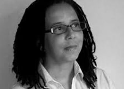 Black and white portrait of a writer with locs and glasses wearing a collared shirt.