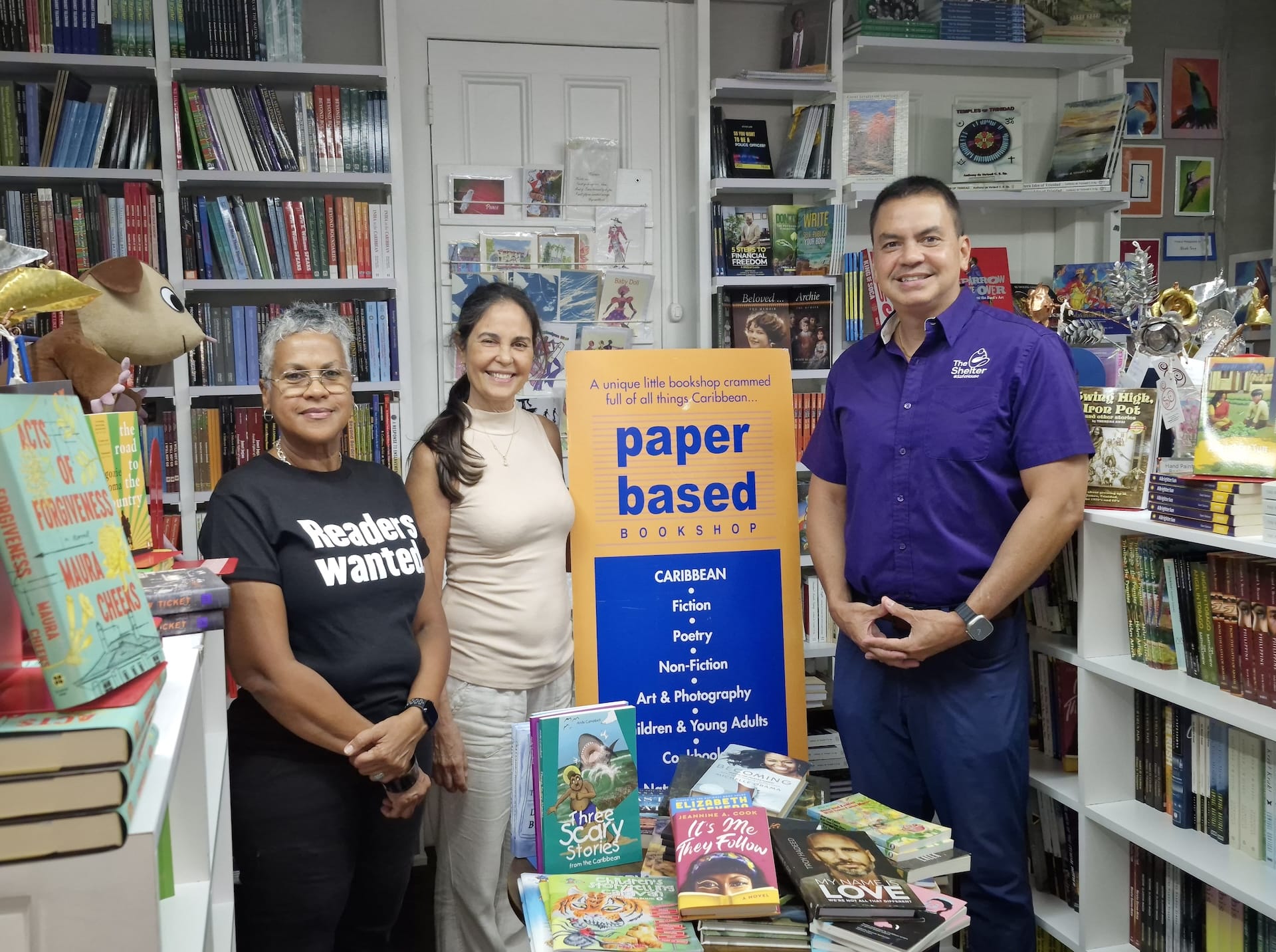 Georgia Popplewell, Managing Director of Bocas Lit Fest, and Simone Camps, Manager of Paper Based Bookshop, hand over donated books to Colin Mitchell, Chairman of The Shelter-A Safe House for Survivors of Domestic Violence, as part of the Books that Build Hope initiative.