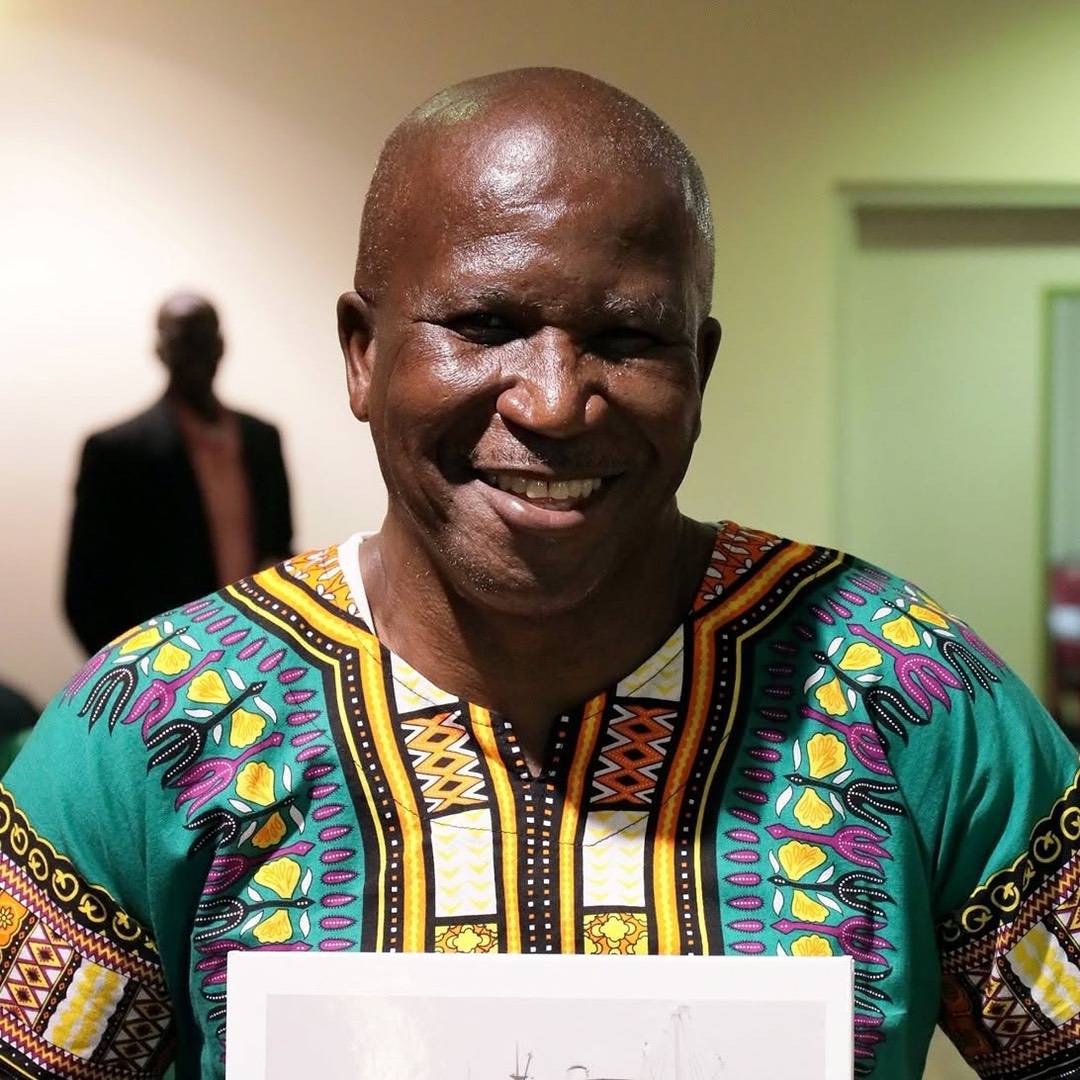 A smiling man wearing a green patterned dashiki shirt.