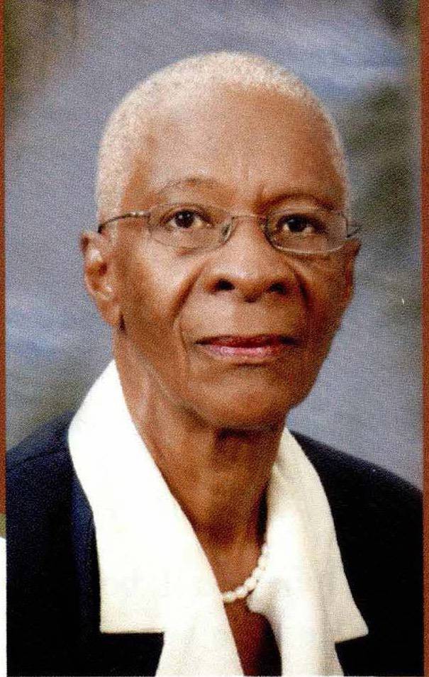 Portrait of an older Black woman with short hair, wearing glasses, a white collared shirt, and a pearl necklace.