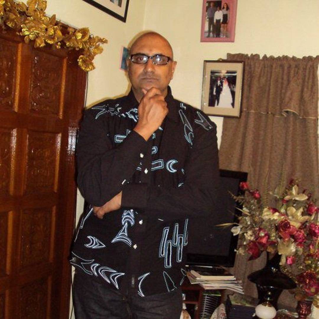 A man in a black button-down shirt with white geometric patterns posing with his hand to his chin.
