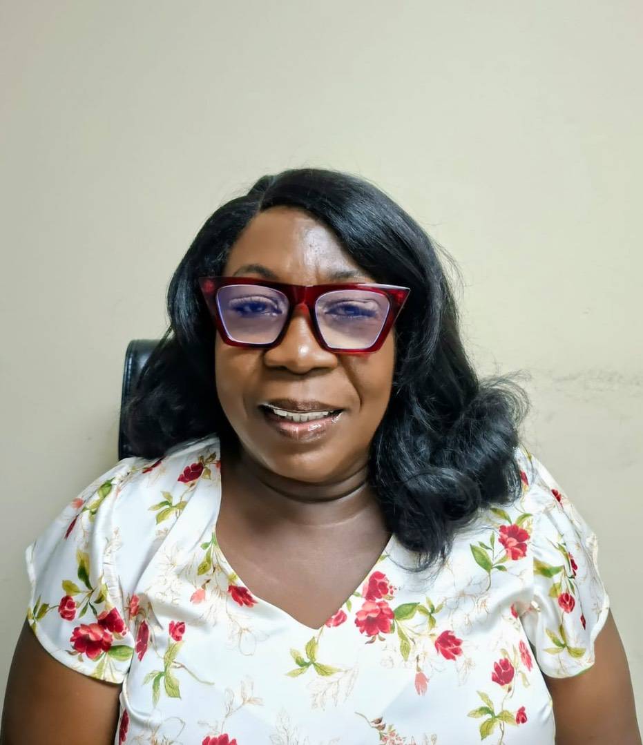 A woman with shoulder-length dark hair wearing red-framed glasses and a white floral blouse.