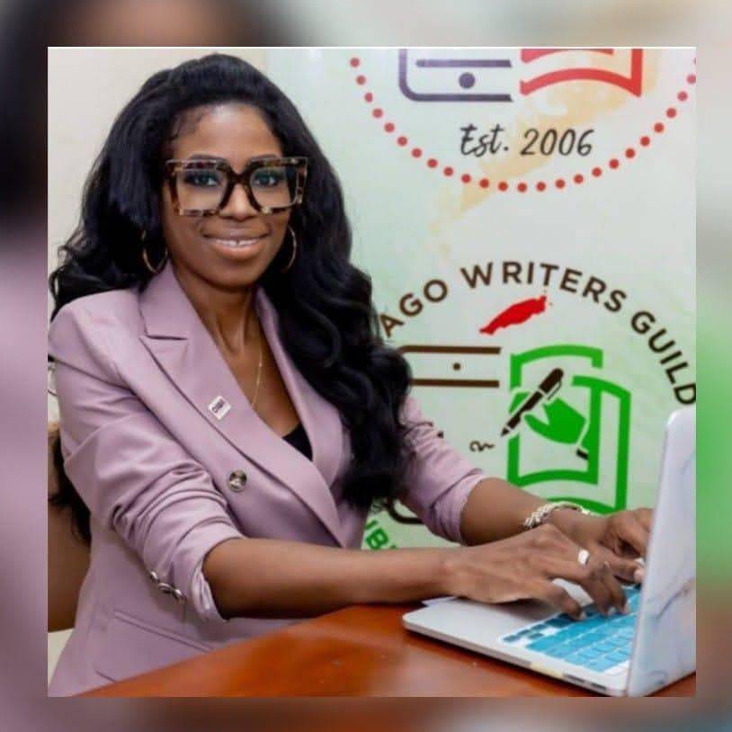 A woman wearing glasses and a light-coloured blazer types on a laptop in front of a Chicago Writers’ Guild logo.