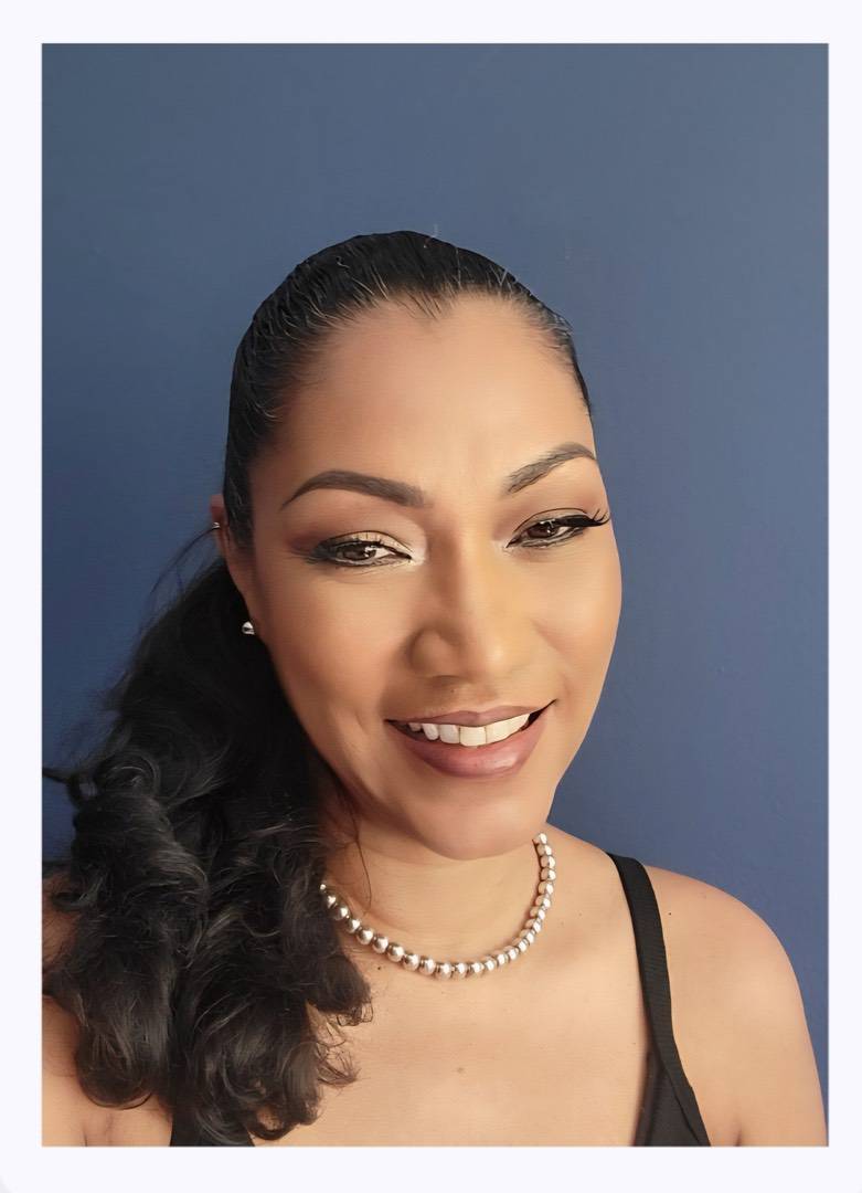 A woman with a ponytail and a pearl necklace smiles at the camera against a blue background.