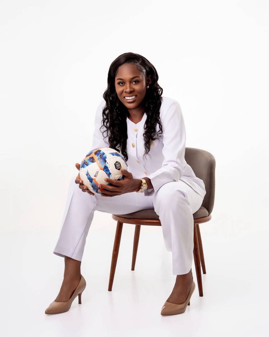 A woman in a white suit sitting on a chair, holding a football.