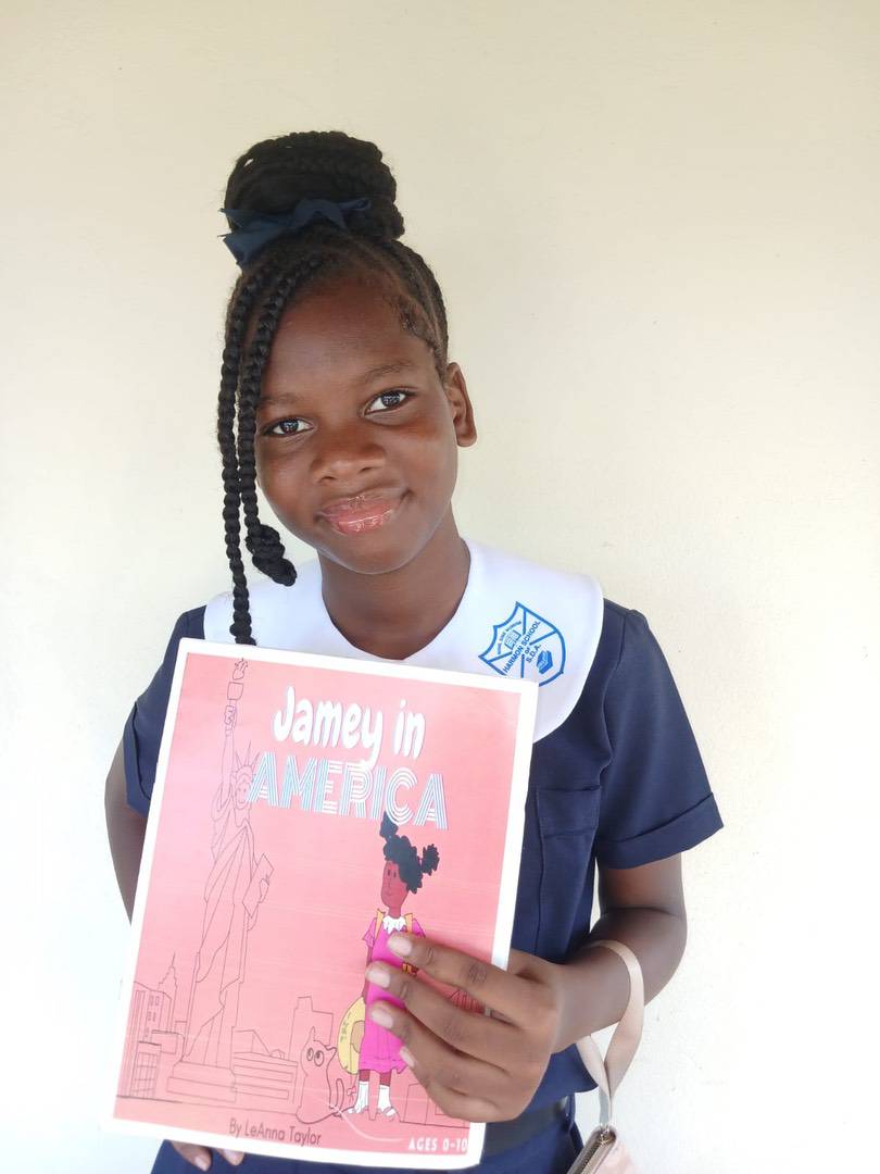 A girl in a school uniform holding a children’s book titled “Jamey in America” by LeAnna Taylor.
